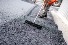 Worker levelling fresh asphalt on a road construction site, indu